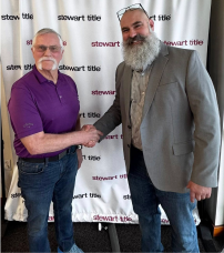 Two men shaking hands in front of a sign that says stewart title