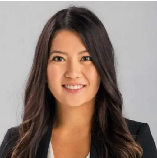 Studio headshot of a smiling woman with long dark hair wearing a black blazer and white top
