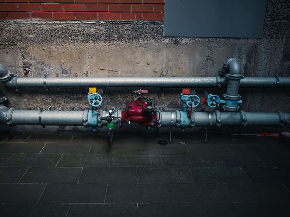Industrial pipes with blue valves and a red pump against a brick wall