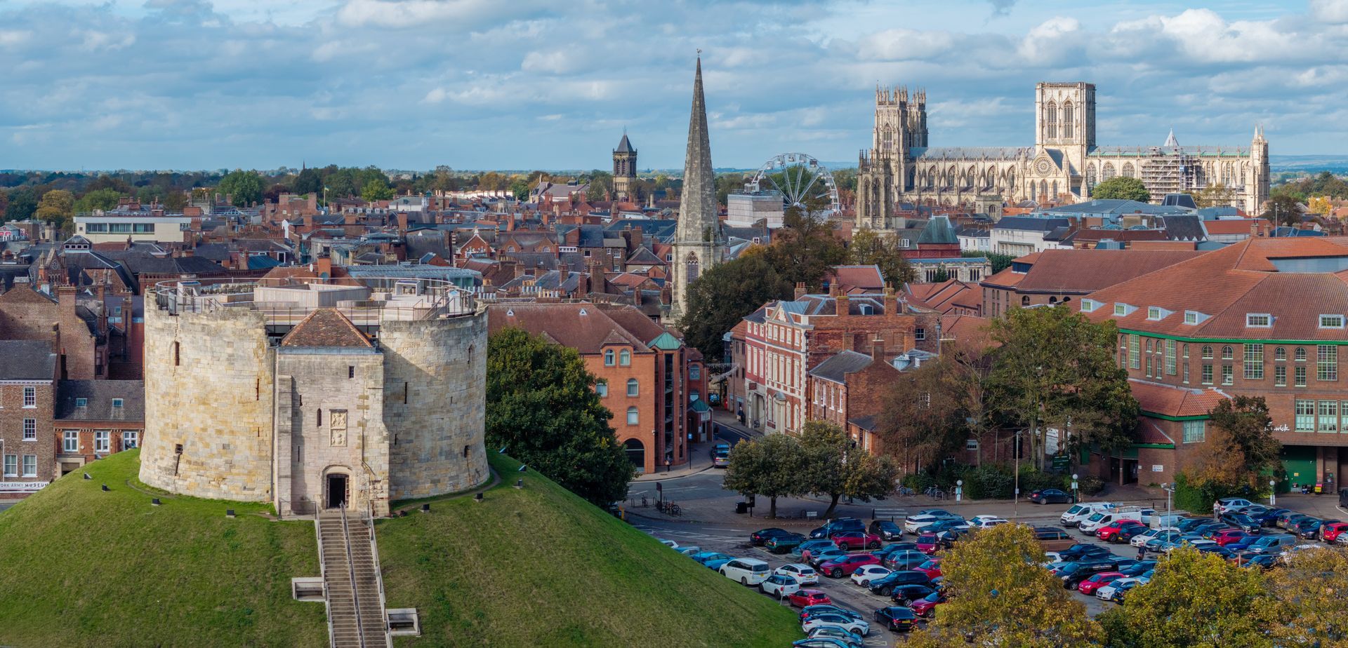 Aerial view of York City, England. Clifford's Tower on a hill, cathedral, and rooftops. Cars are parked below.