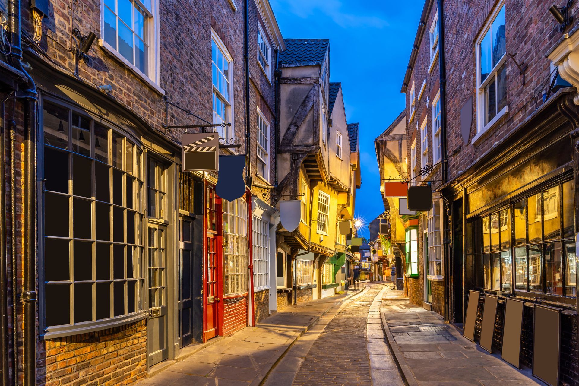 Narrow cobblestone street with historic buildings, lit by streetlights at dusk.