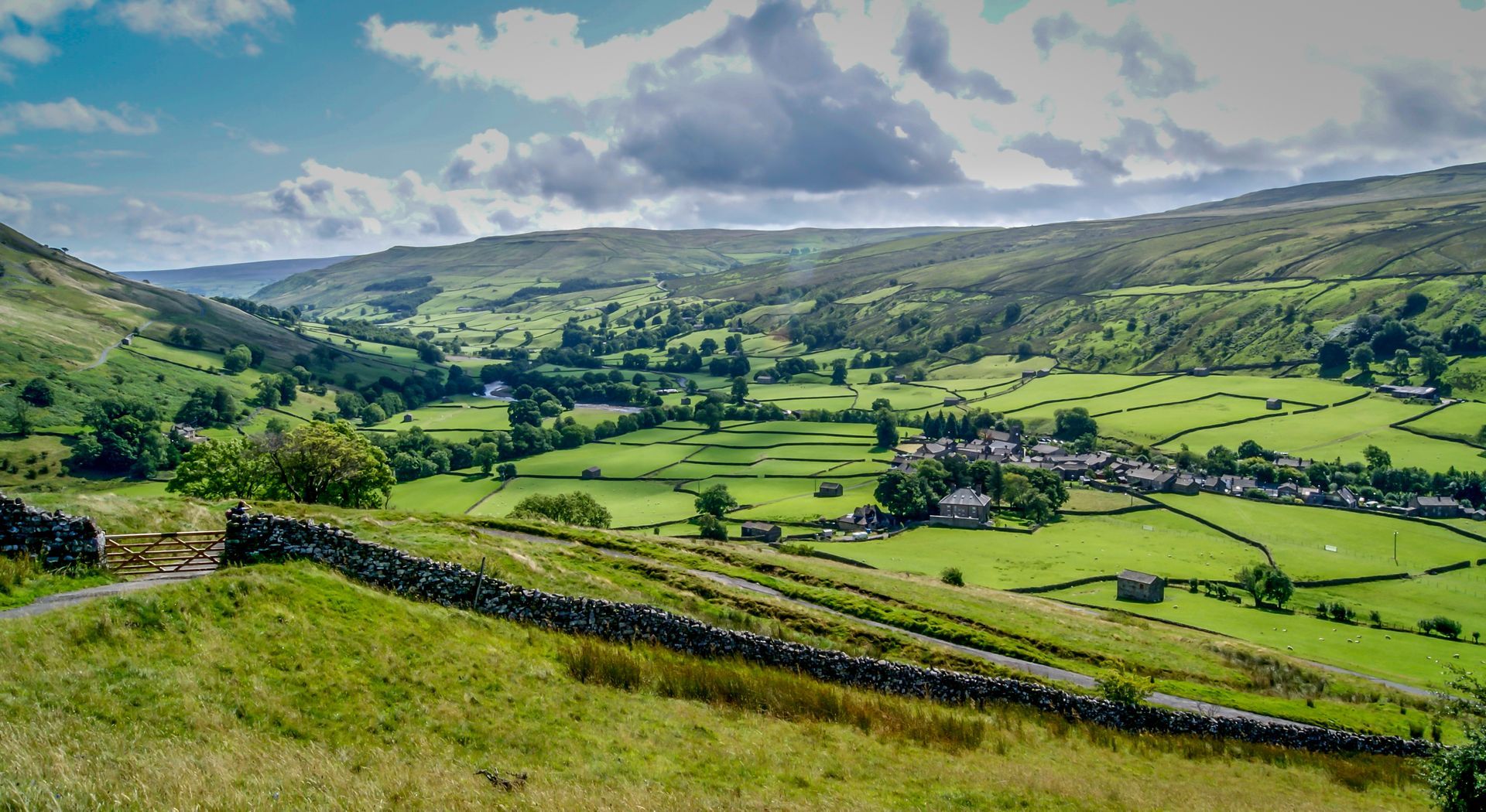 Rolling green hills and valley with a village nestled below a cloudy sky.