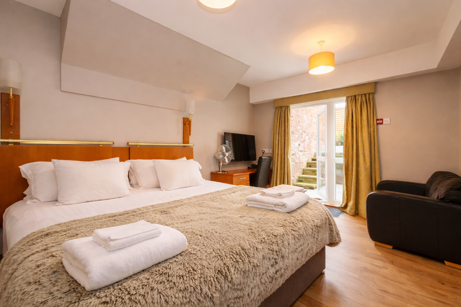 A hotel room with a bed, television, and armchair; doorway to a small patio.