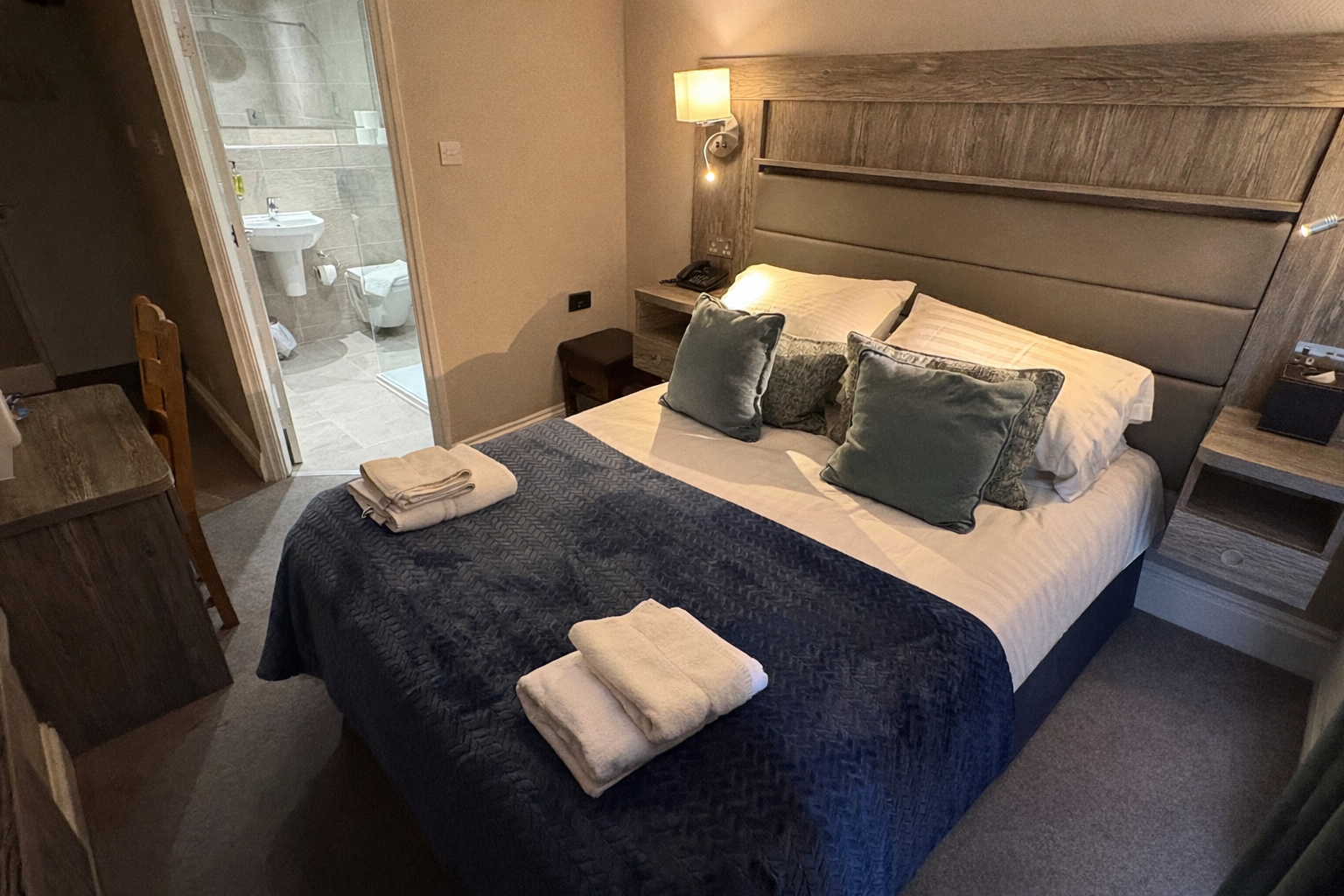 Hotel bedroom with a double bed, bathroom visible through the doorway, neutral colors.