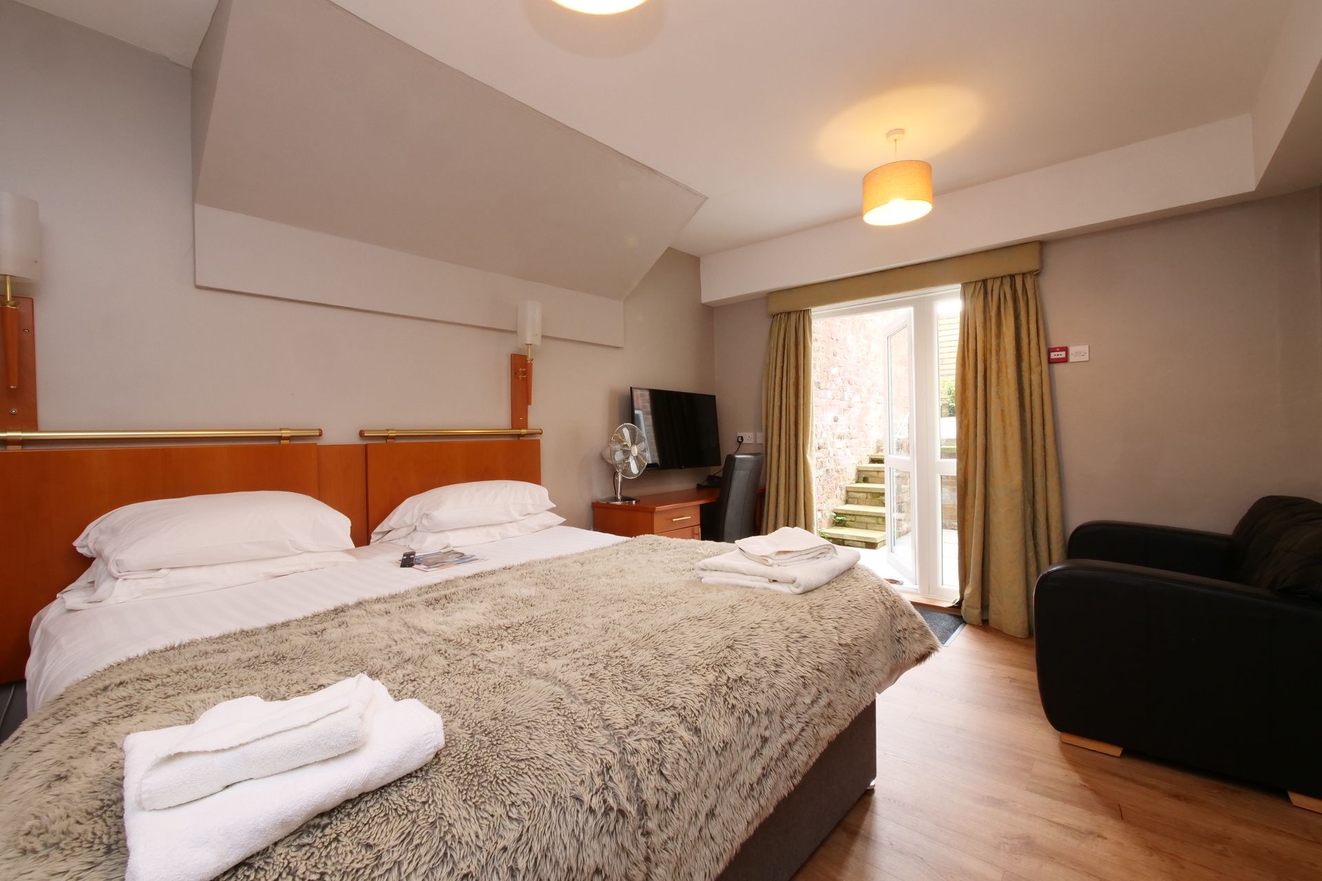 A hotel room with a bed, television, and armchair; doorway to a small patio.