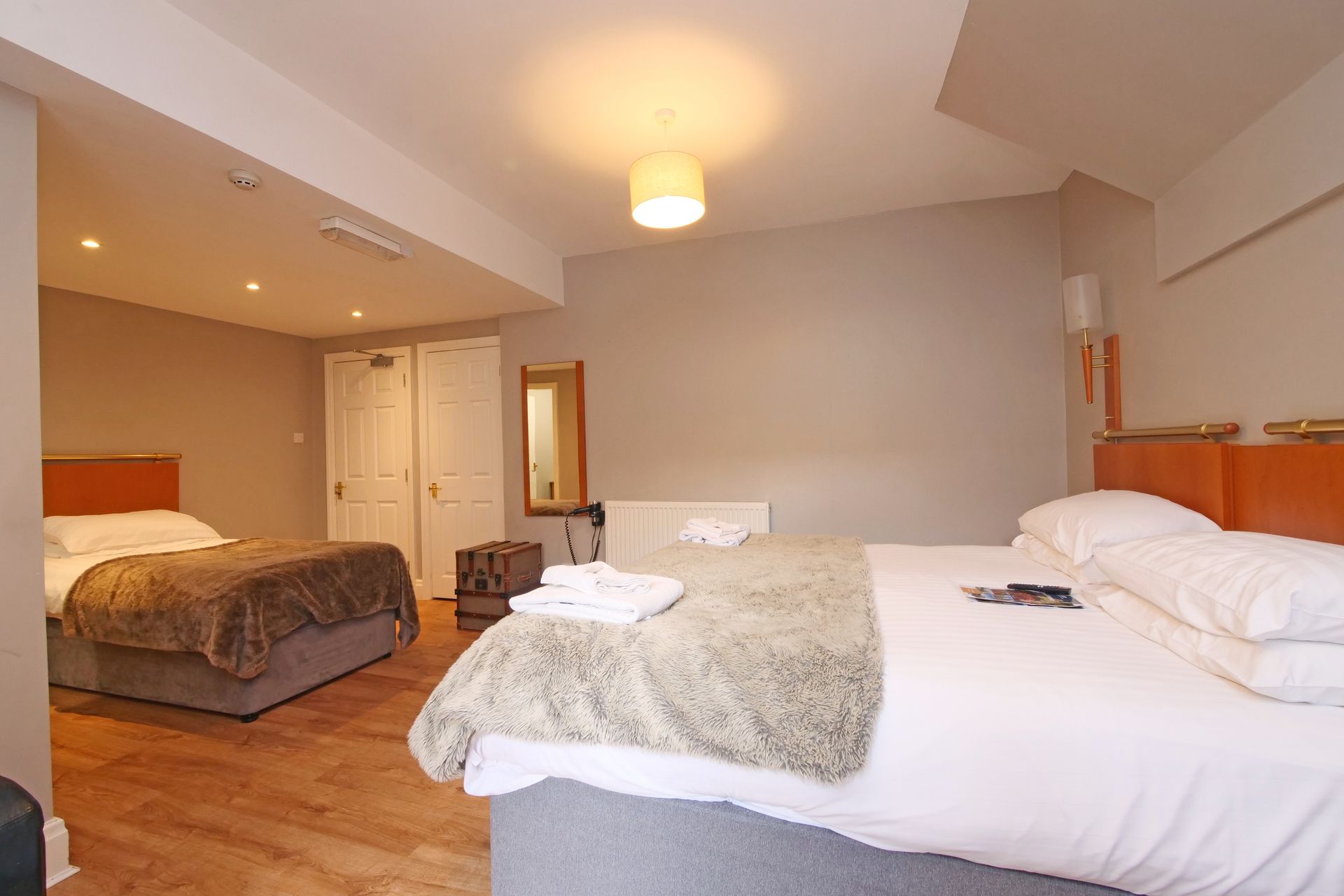 Hotel room with two beds, neutral walls, wooden floors, and a warm, inviting ambiance.