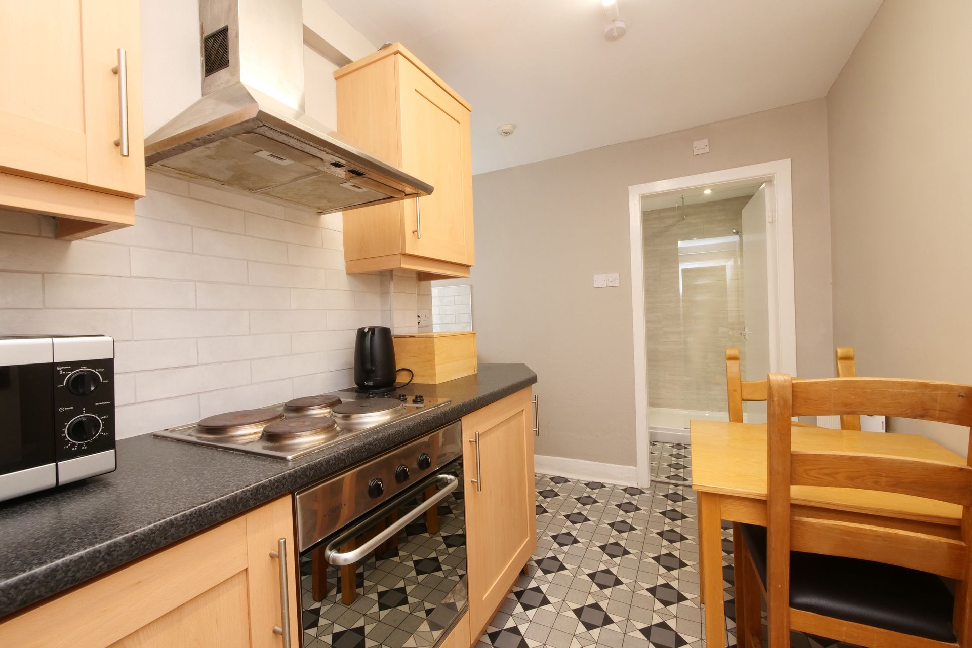 Kitchen with light wood cabinets, black countertops, and patterned floor; open door leads to a hallway.
