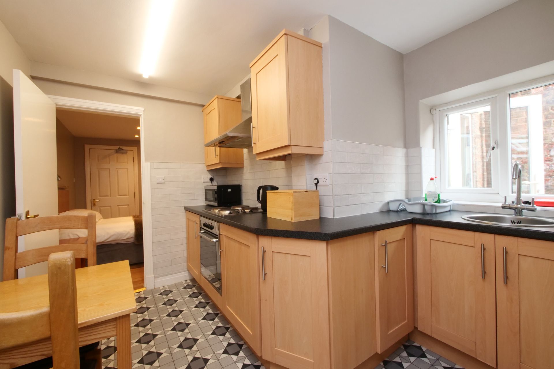 Kitchen with light wood cabinets, black countertop, and tiled floor. Open doorway leads to bedroom.