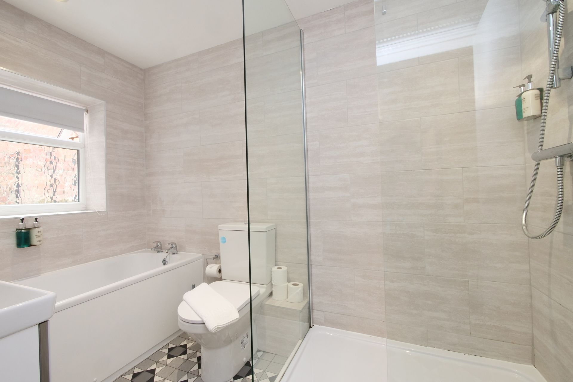 Modern bathroom with white fixtures, glass shower, and neutral tile.
