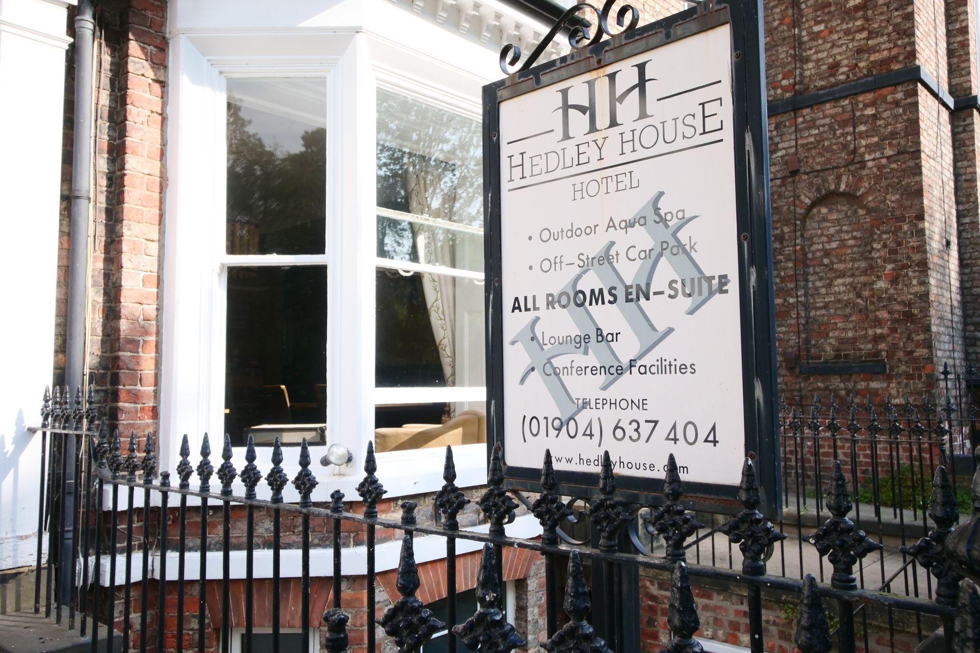 Sign for Hedley House Hotel, York. Black and white, in front of a brick building and black wrought iron fence.