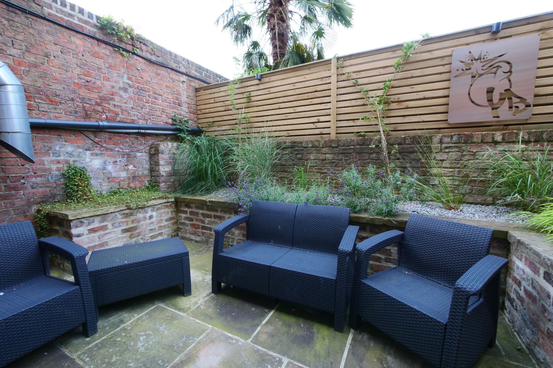 Outdoor seating area with black wicker furniture, brick walls, and wooden fence.