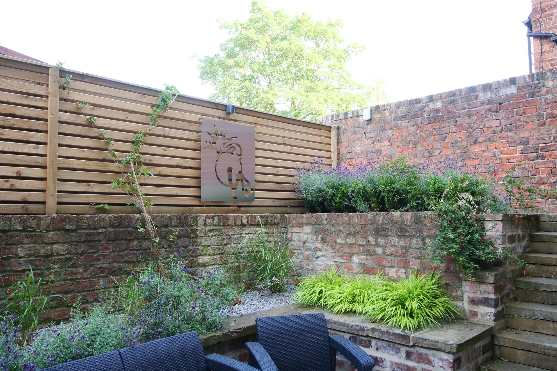 A small garden with tiered brick walls, wooden fence, and metal artwork.