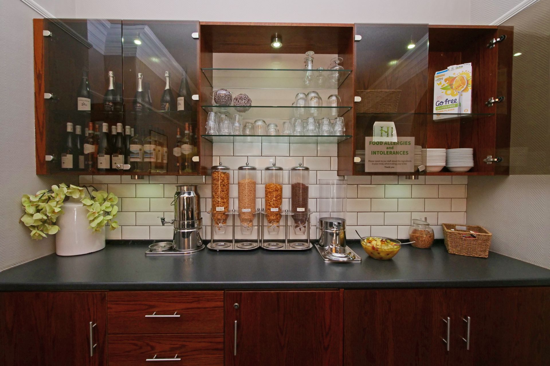 Breakfast bar with cereal dispensers, glassware, and cabinets filled with food and drink.