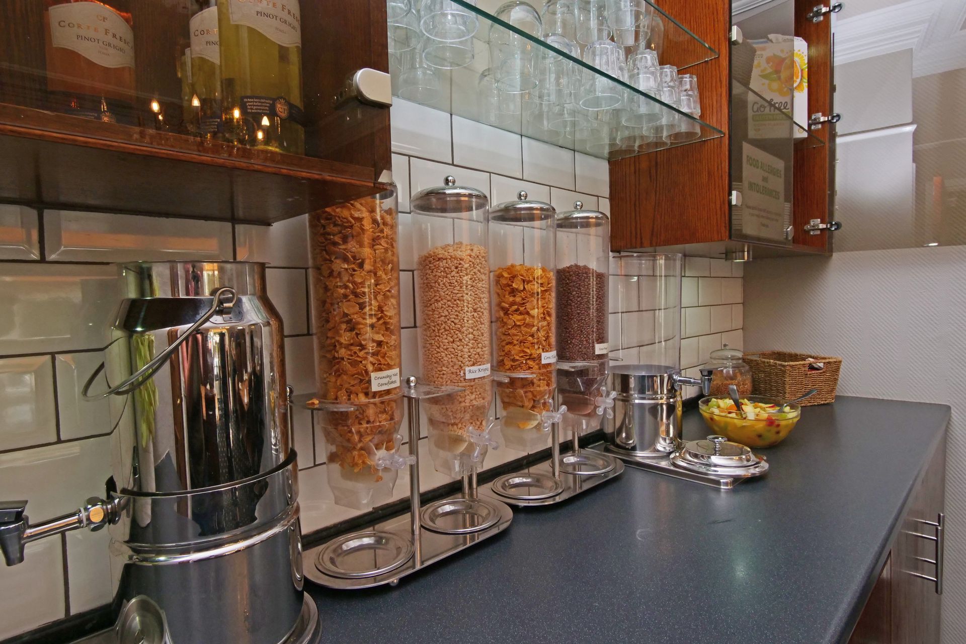 Breakfast buffet counter with cereal dispensers, a coffee urn, and cabinets.