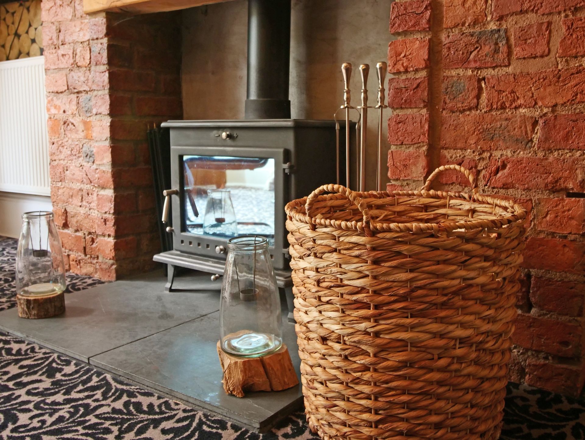 Fireplace with brick surround, metal stove, wood basket, and glass candle holders.