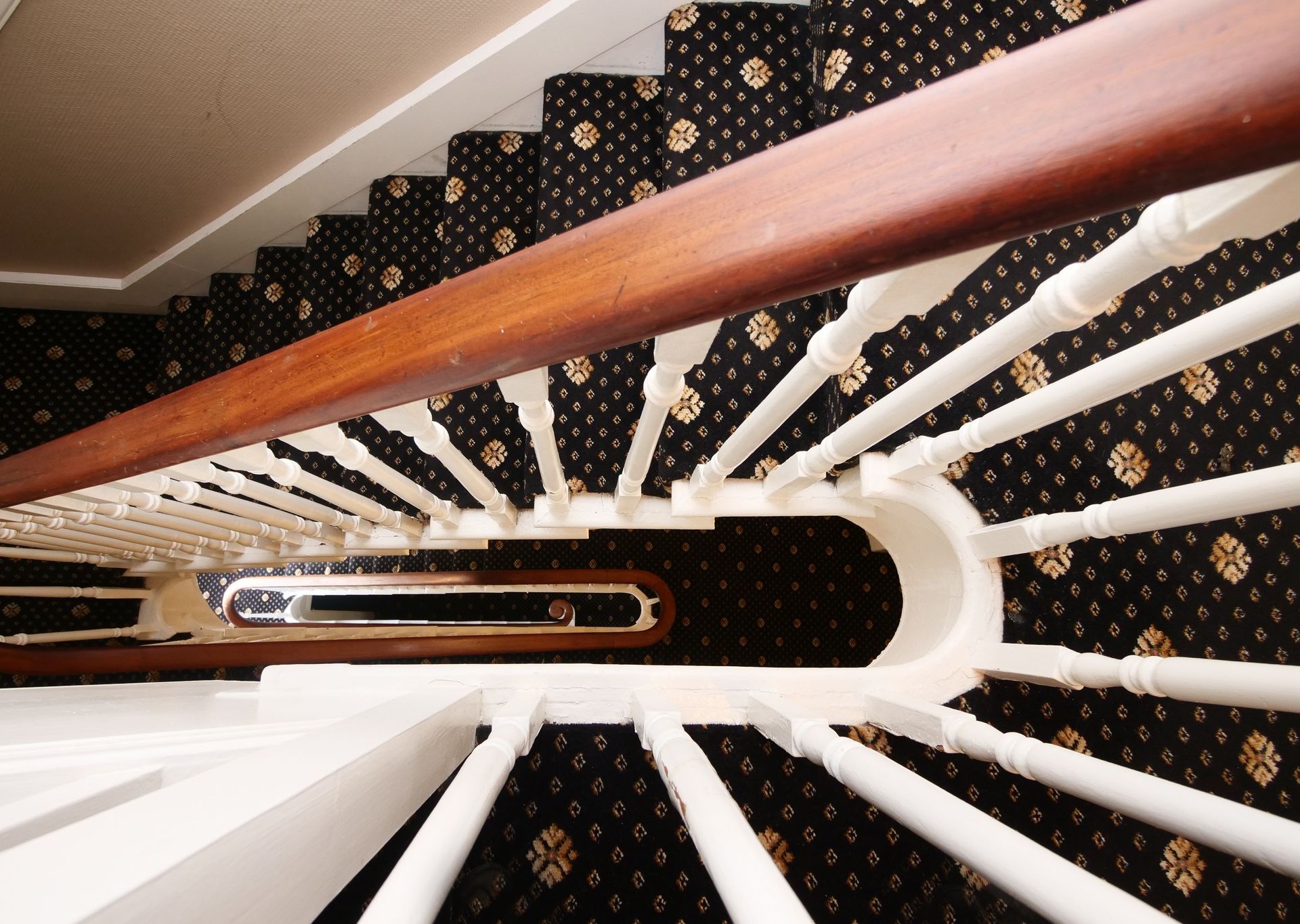 Looking down a staircase with brown handrail and white balusters, carpeted steps.