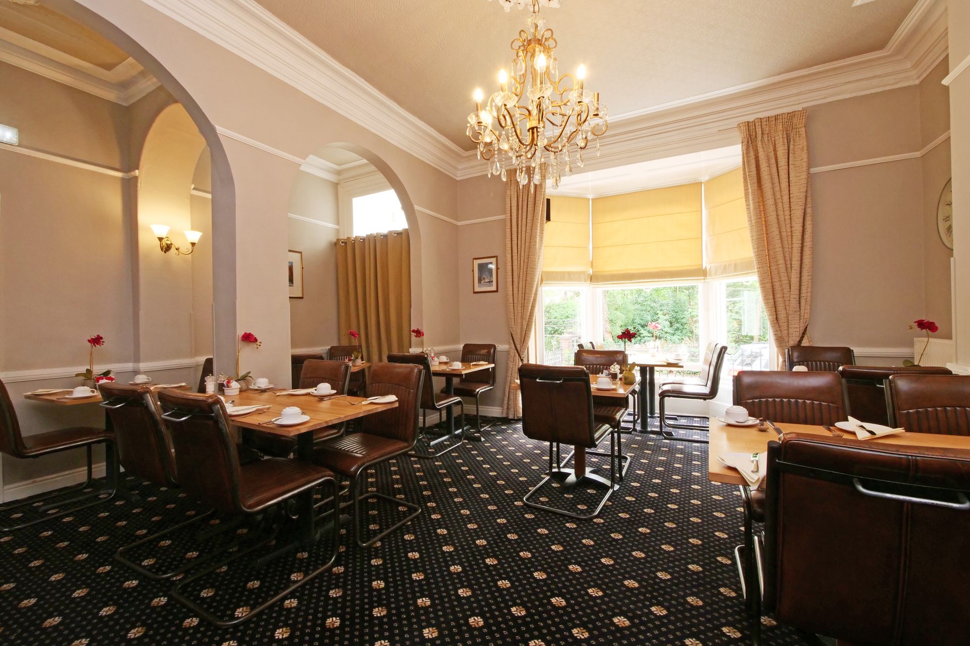 A hotel breakfast room with tables, chairs, floral arrangements, and a chandelier.