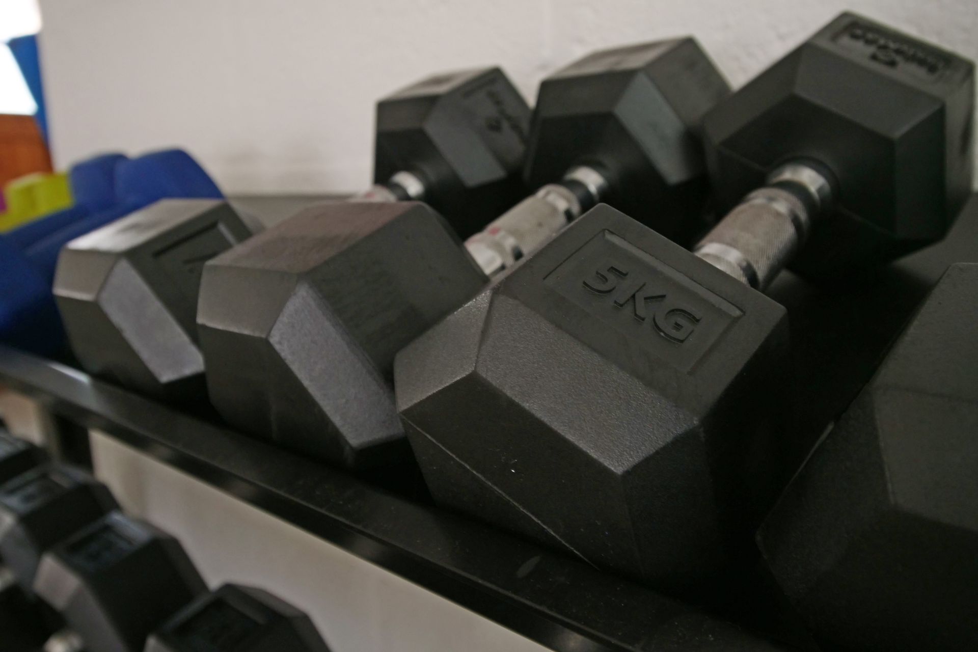 Black hexagonal dumbbells on a weight rack. Each dumbbell is marked 