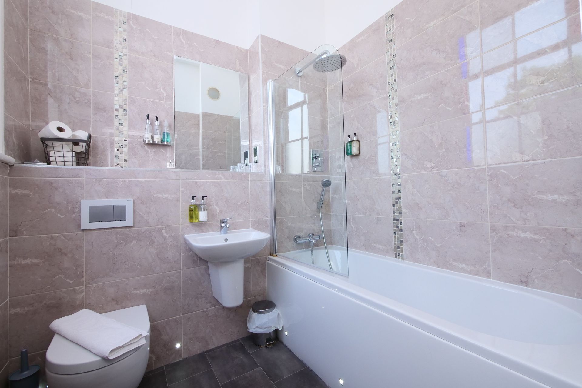 Bathroom with white fixtures, gray tiled walls, and a glass shower door.