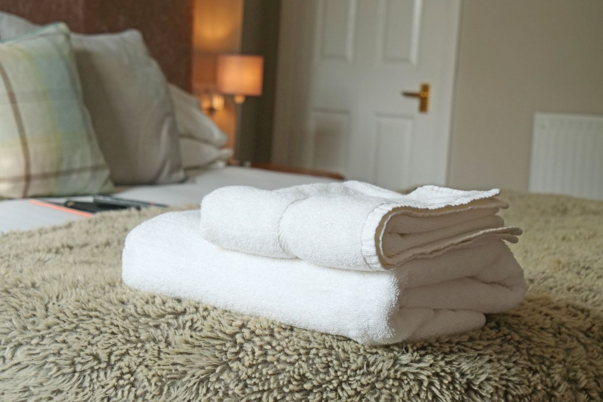 White towels folded on a bed with pillows and a door in the background.