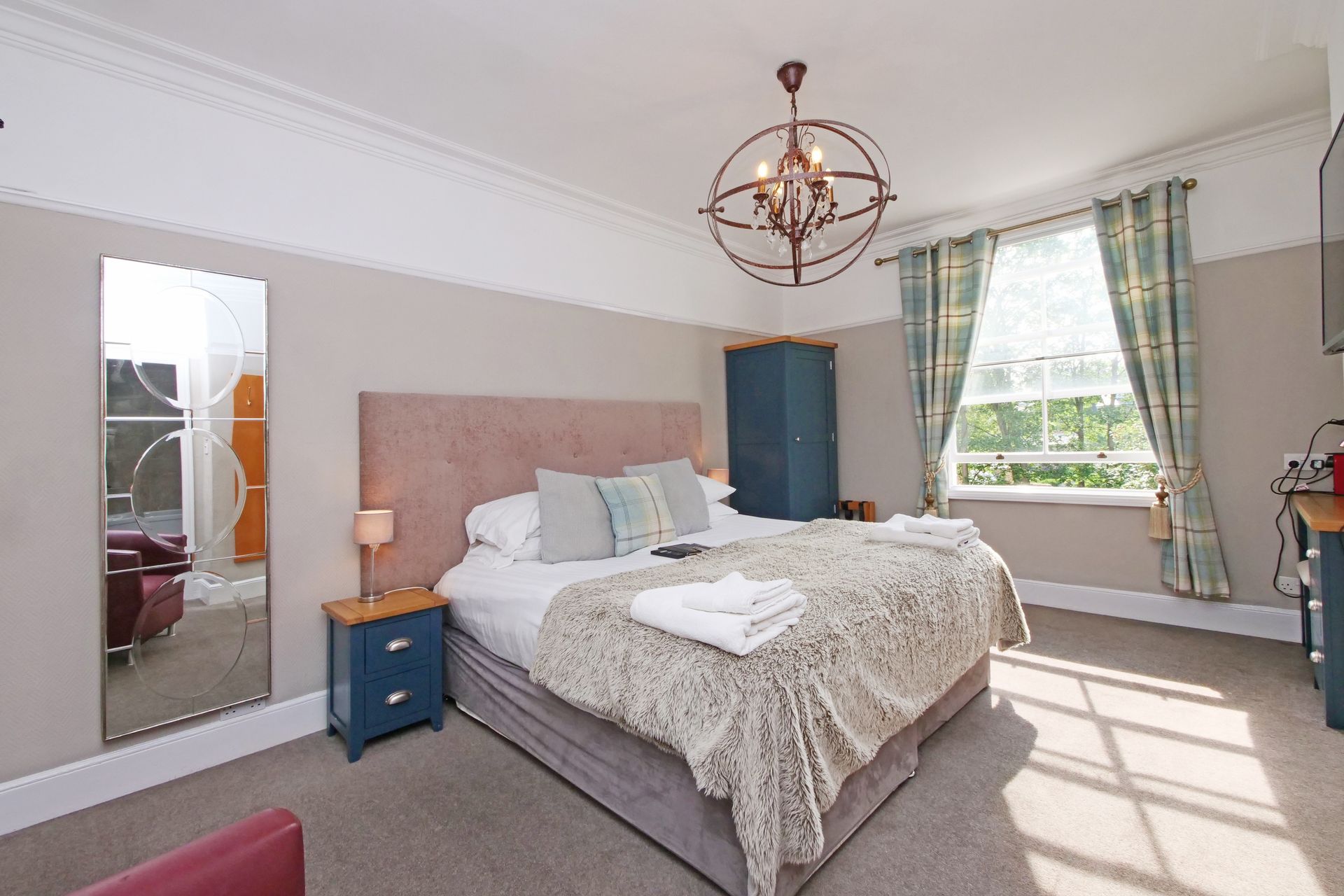 Bedroom with bed, mirror, window, blue furniture, and ornate chandelier.