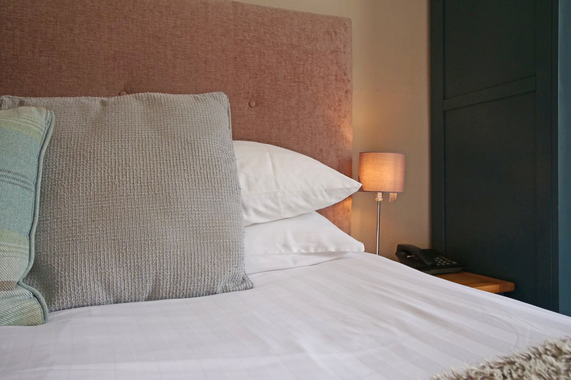 Bed with white sheets, pillows, textured headboard, bedside lamp, and a teal pillow.