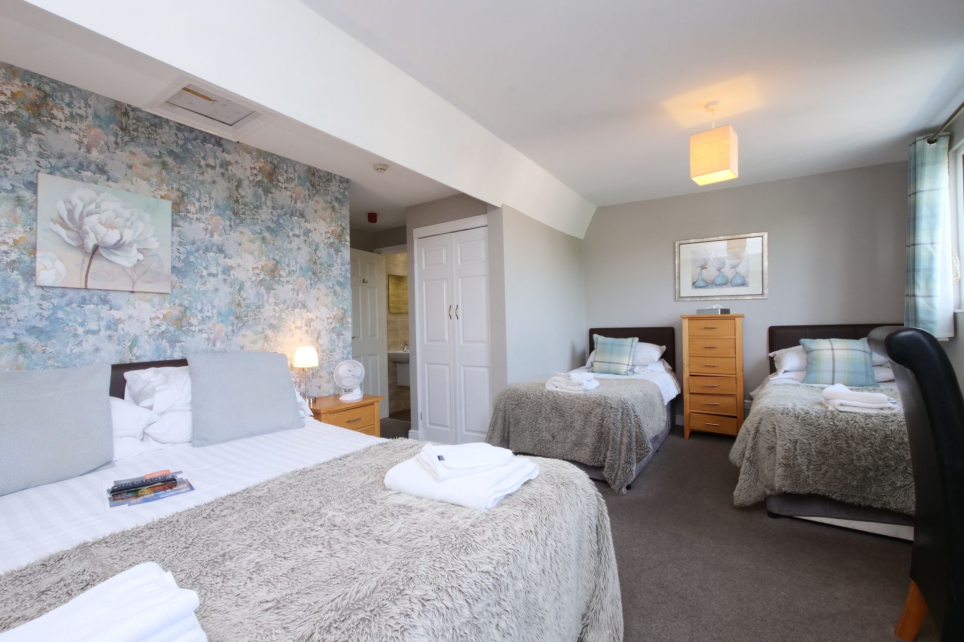 A hotel room with one double bed and two single beds, with floral wallpaper.