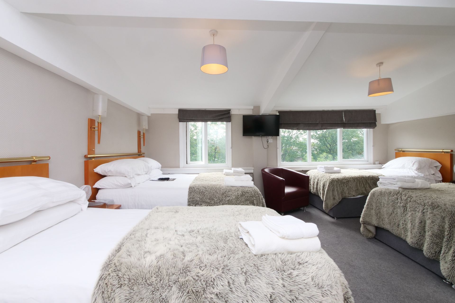 Bedroom with four beds, a small chair, a TV, and two windows.
