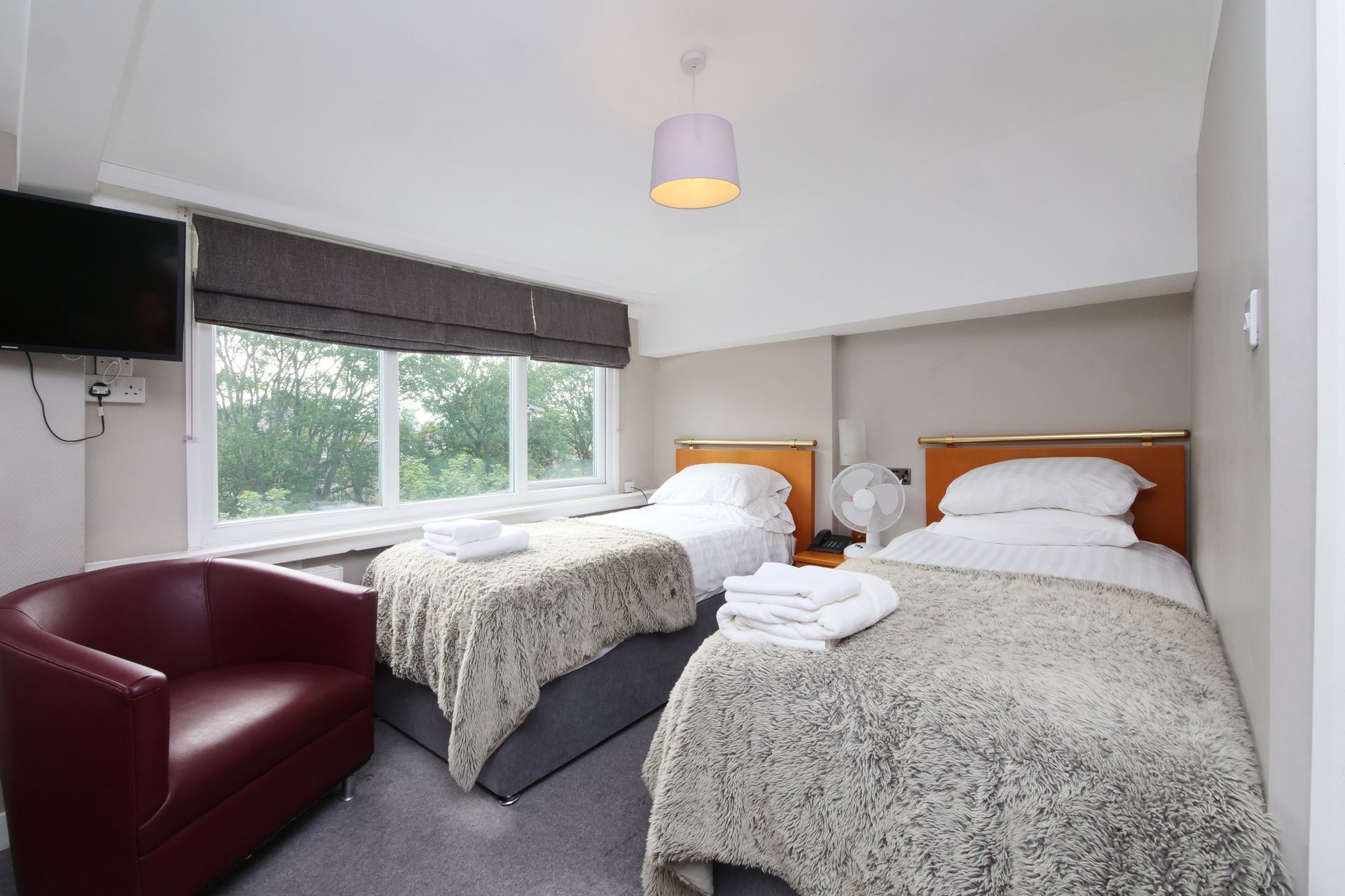 Twin bedroom with two beds, red armchair, TV, and large window with natural light.