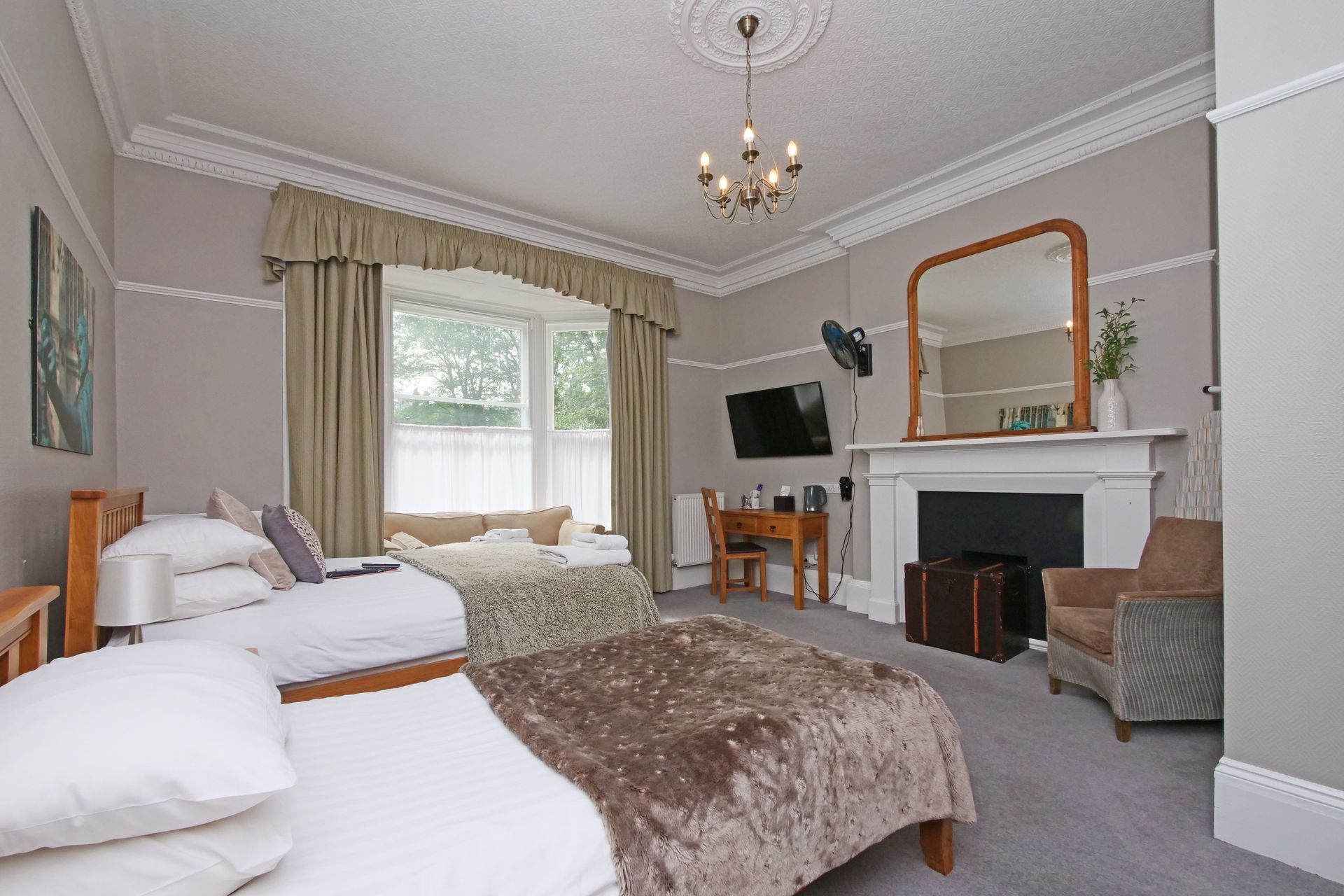 Spacious bedroom with two beds, fireplace, armchair, TV, and large window; neutral tones.