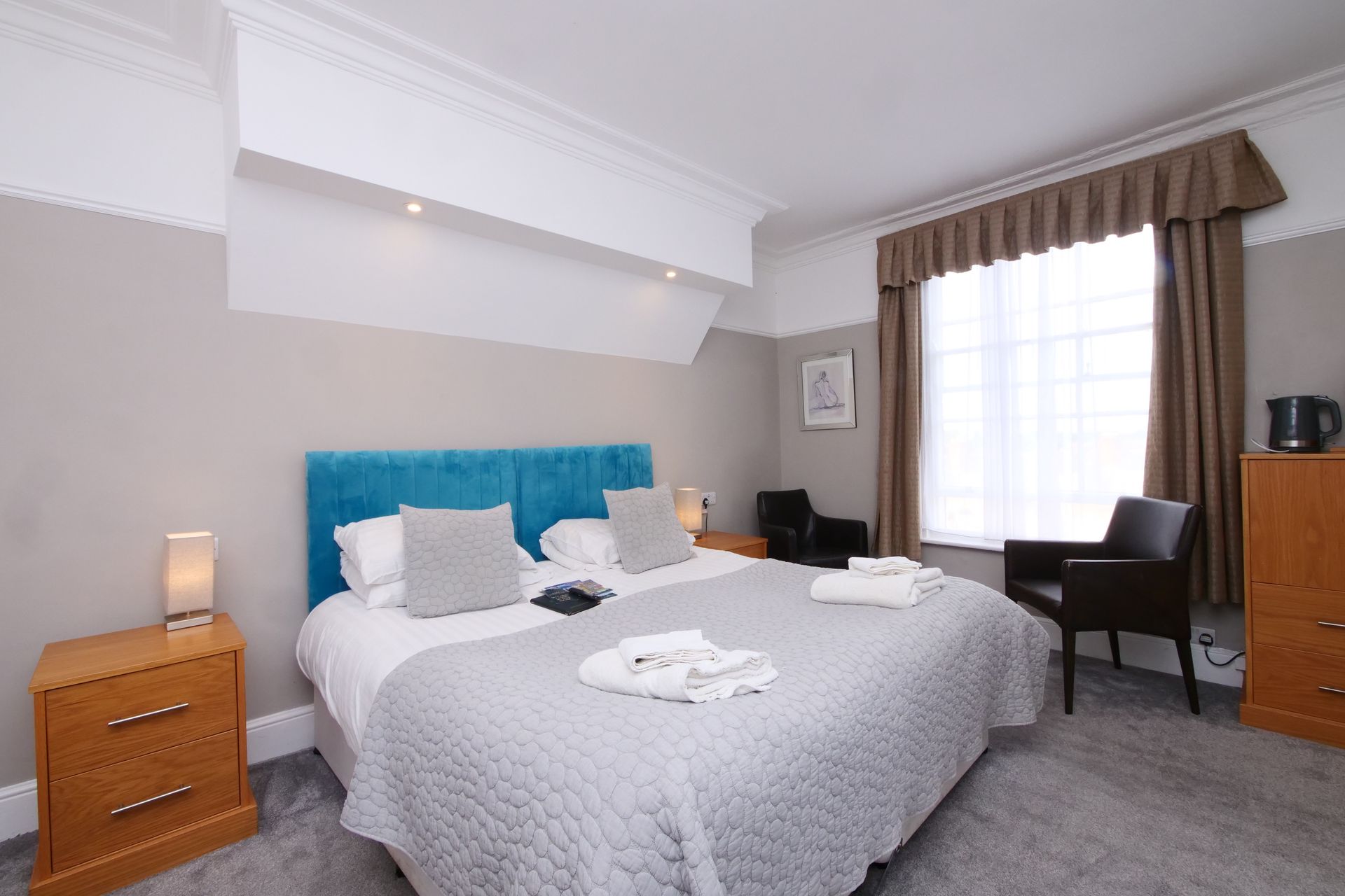 Bedroom with a queen bed, blue headboard, gray bedding, wooden furniture, and a window with curtains.