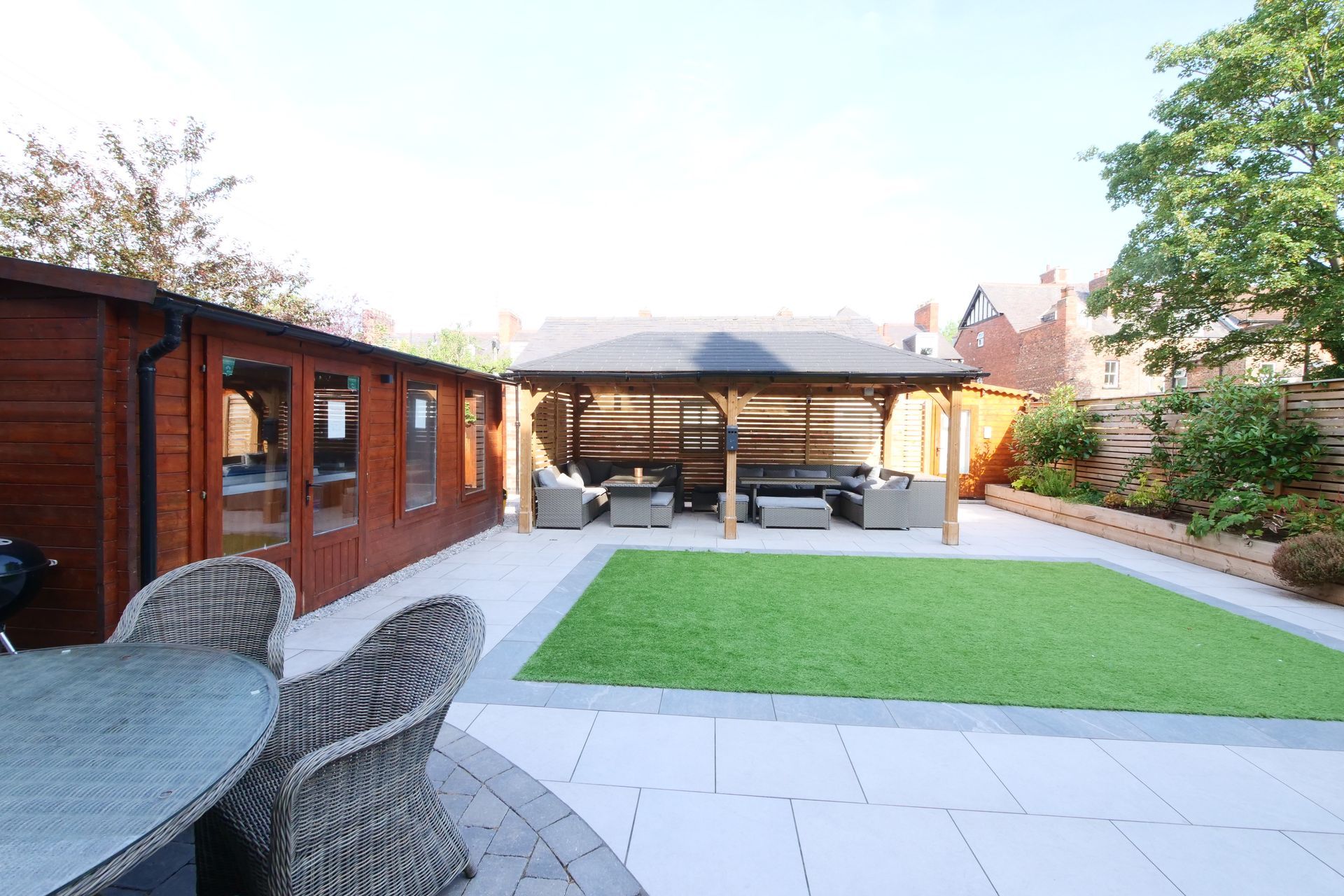 Patio with gazebo, shed, artificial lawn, seating. Sunny outdoor setting.