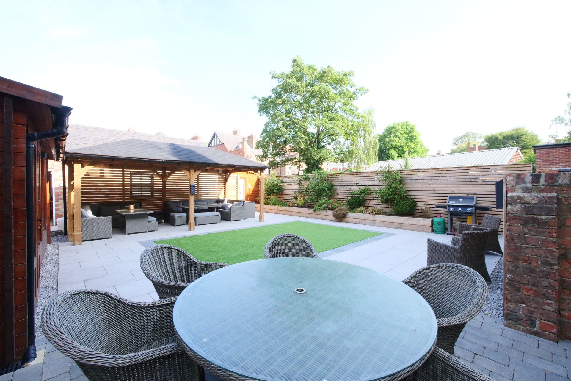 Backyard patio with gray table and chairs, gazebo with seating, and artificial grass.