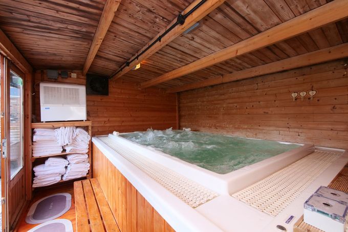 Indoor hot tub with wooden paneling and towels on shelves.