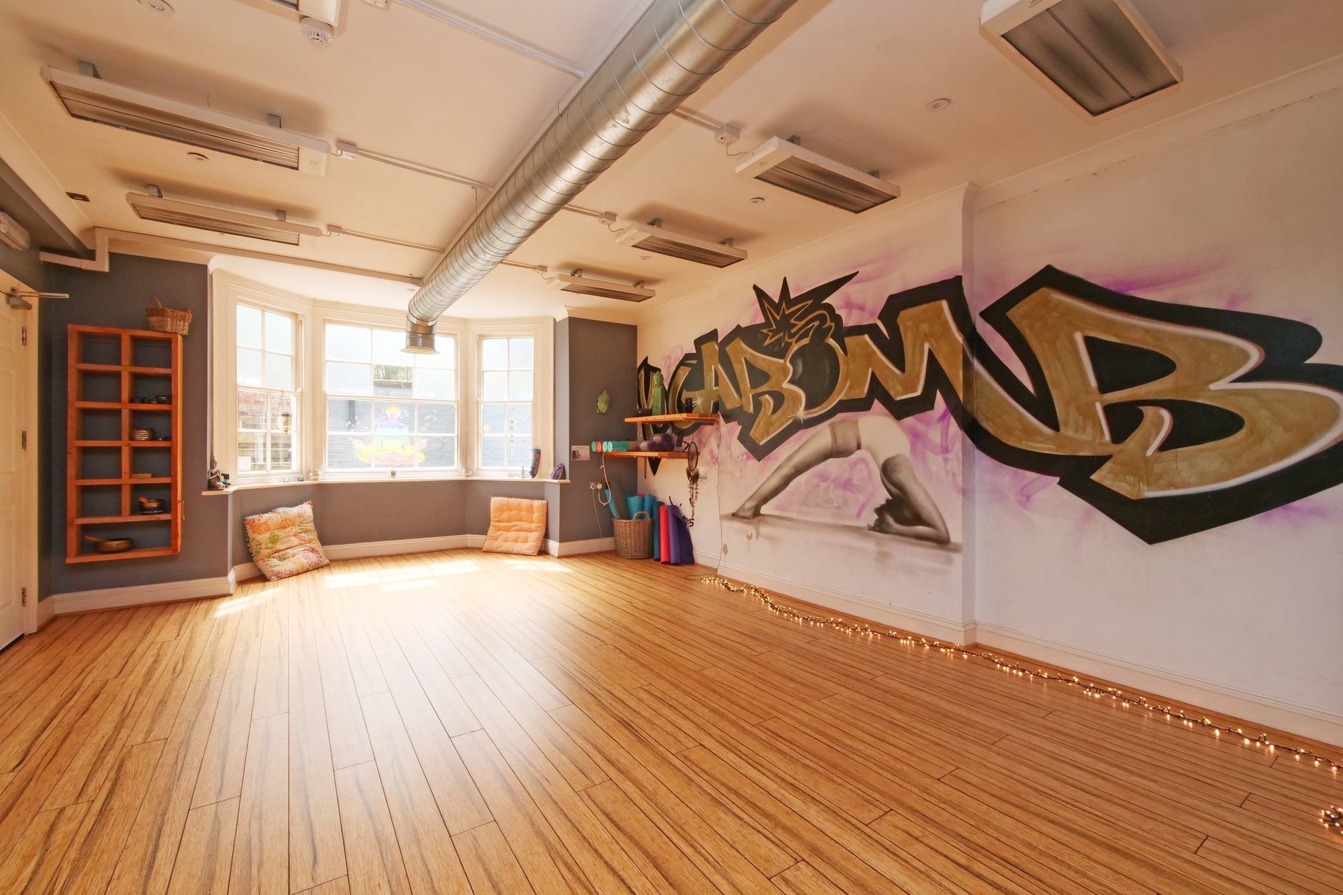 Empty yoga studio with graffiti on the wall, wooden floor, and bright lights.