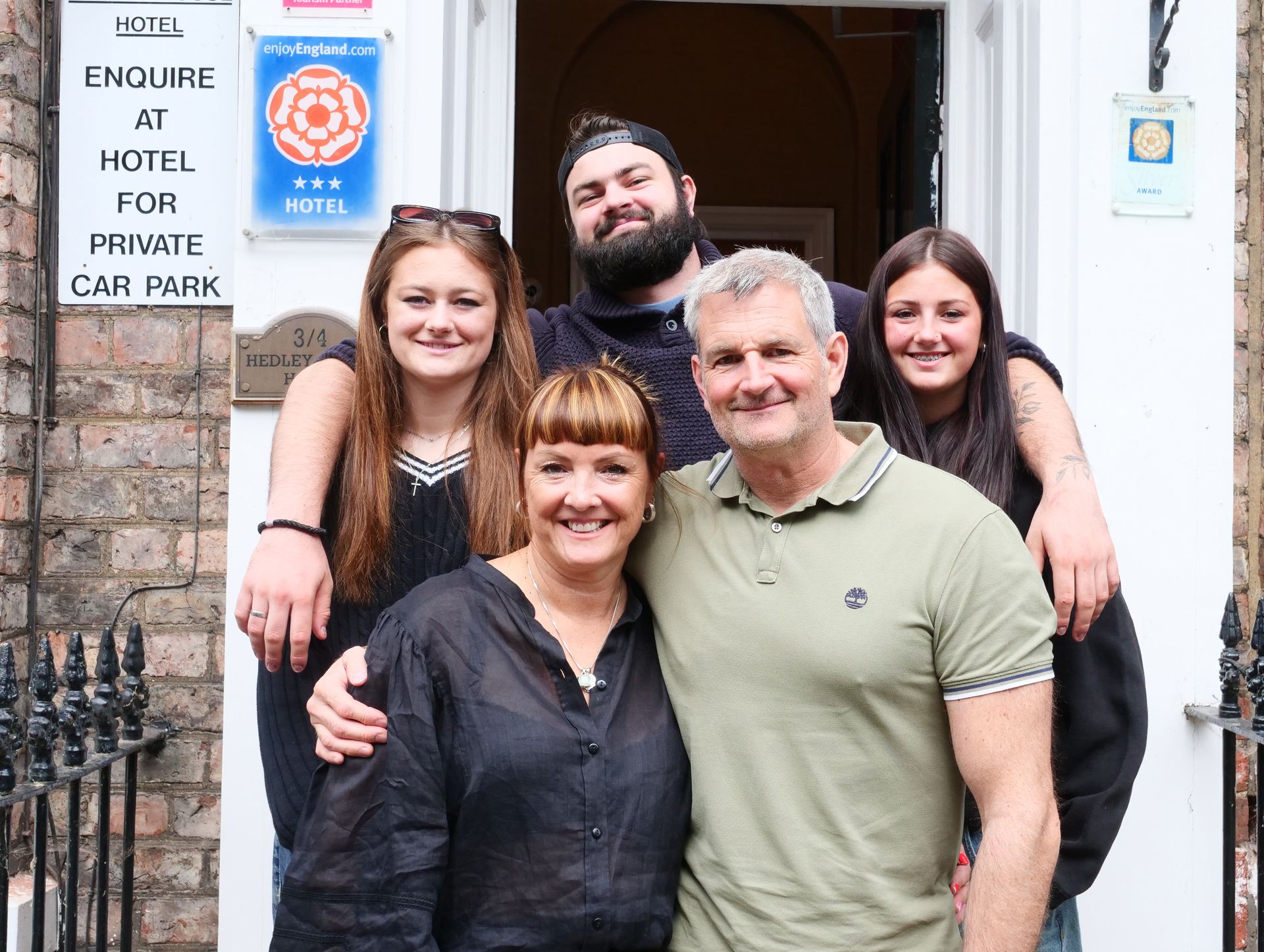 Family of five smiling in front of a hotel entrance.