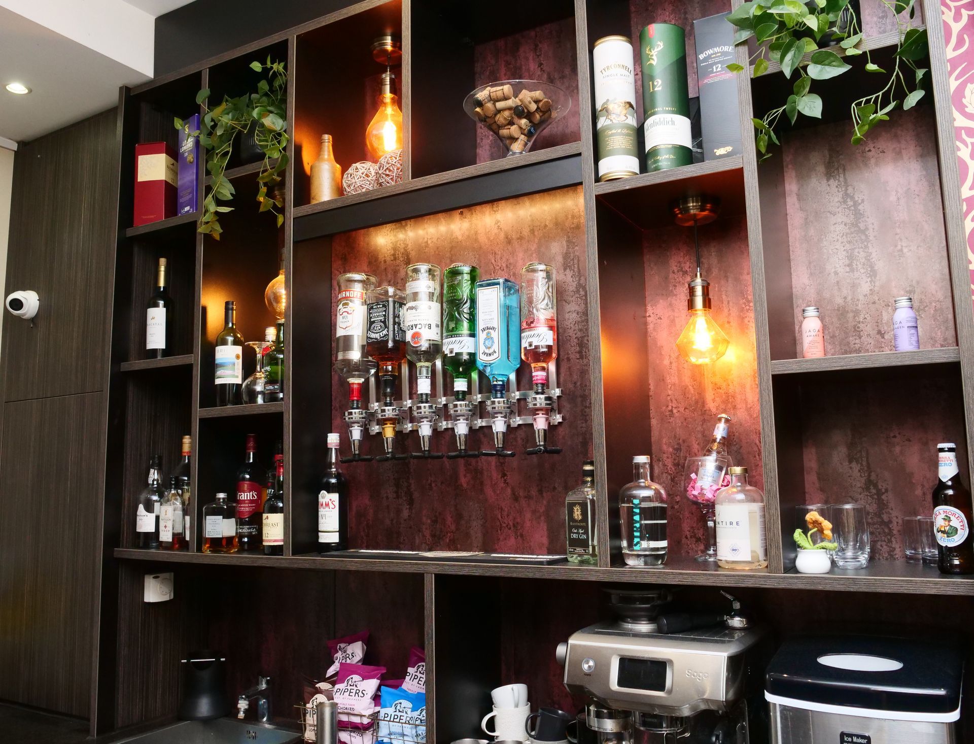 Bar interior with liquor bottles on shelves, drink dispensers, and a coffee machine.