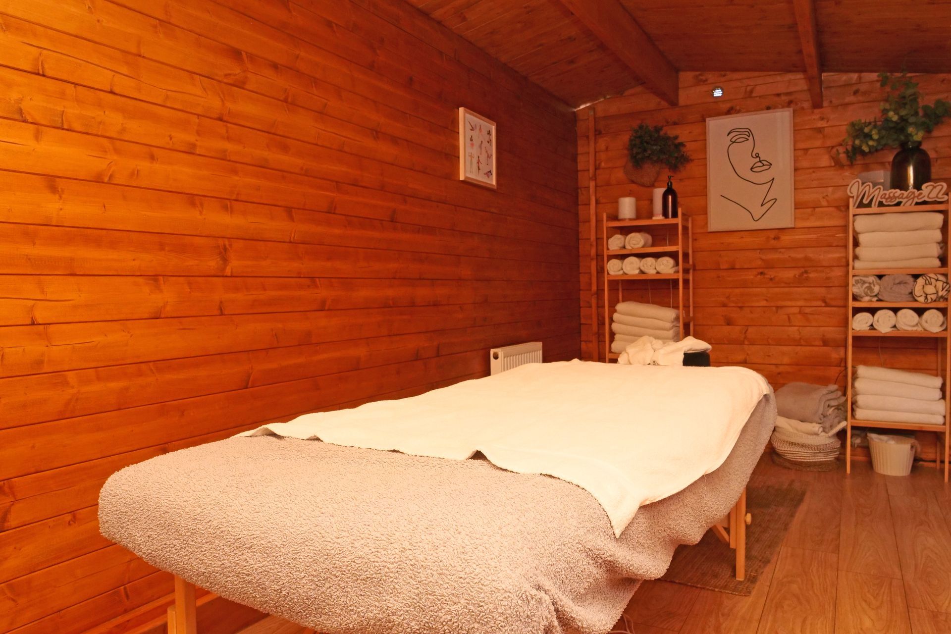 Massage room with wooden walls, massage table, shelves with towels, and plant decor.