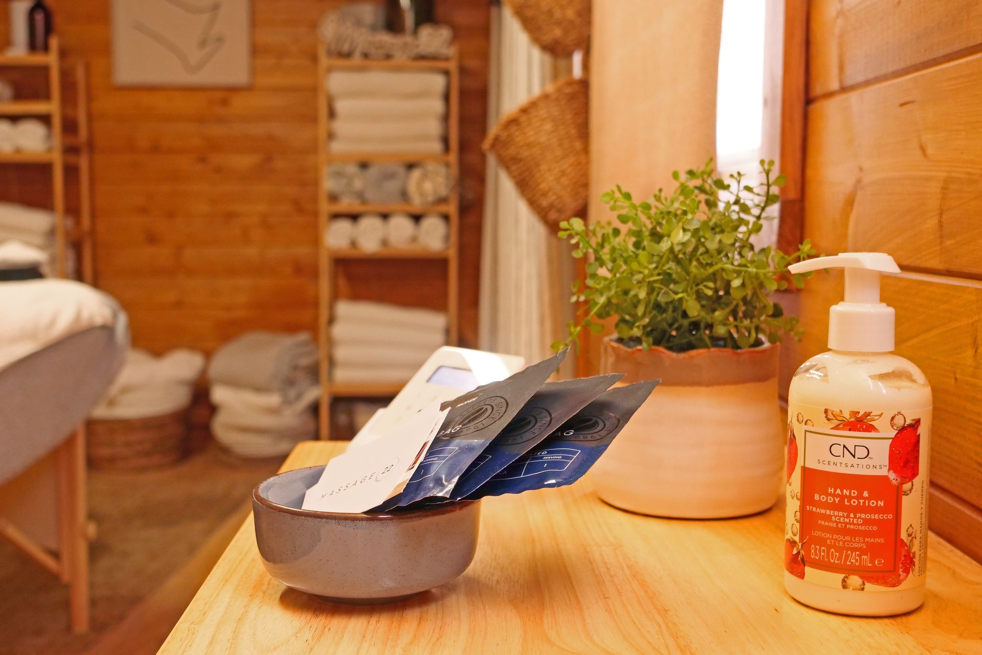 A spa interior with towels on a wooden shelf, a bowl with packets, and a soap bottle.