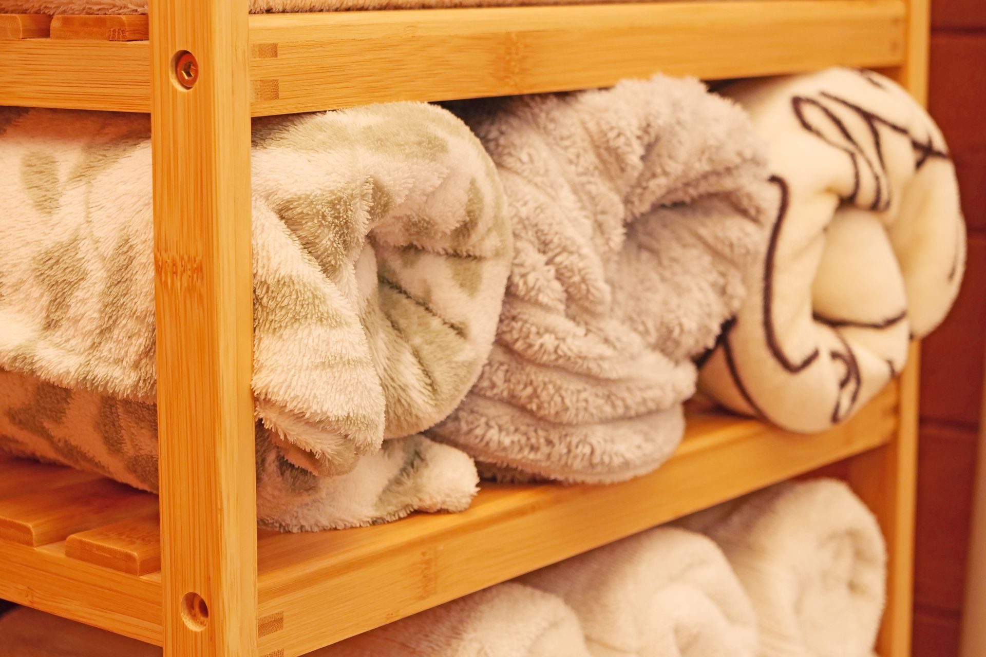 Wooden shelf with rolled towels in shades of white, gray, and green.