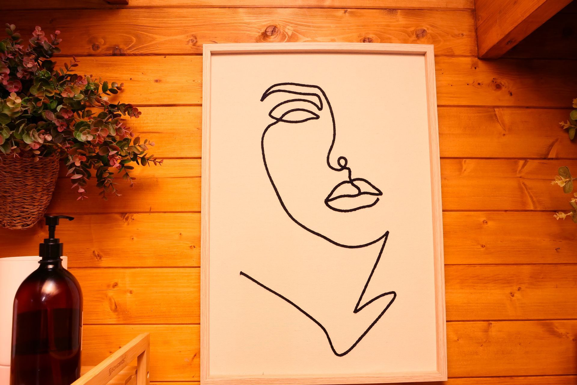 Line drawing of a woman's face in black on white, framed on a wood-paneled wall.