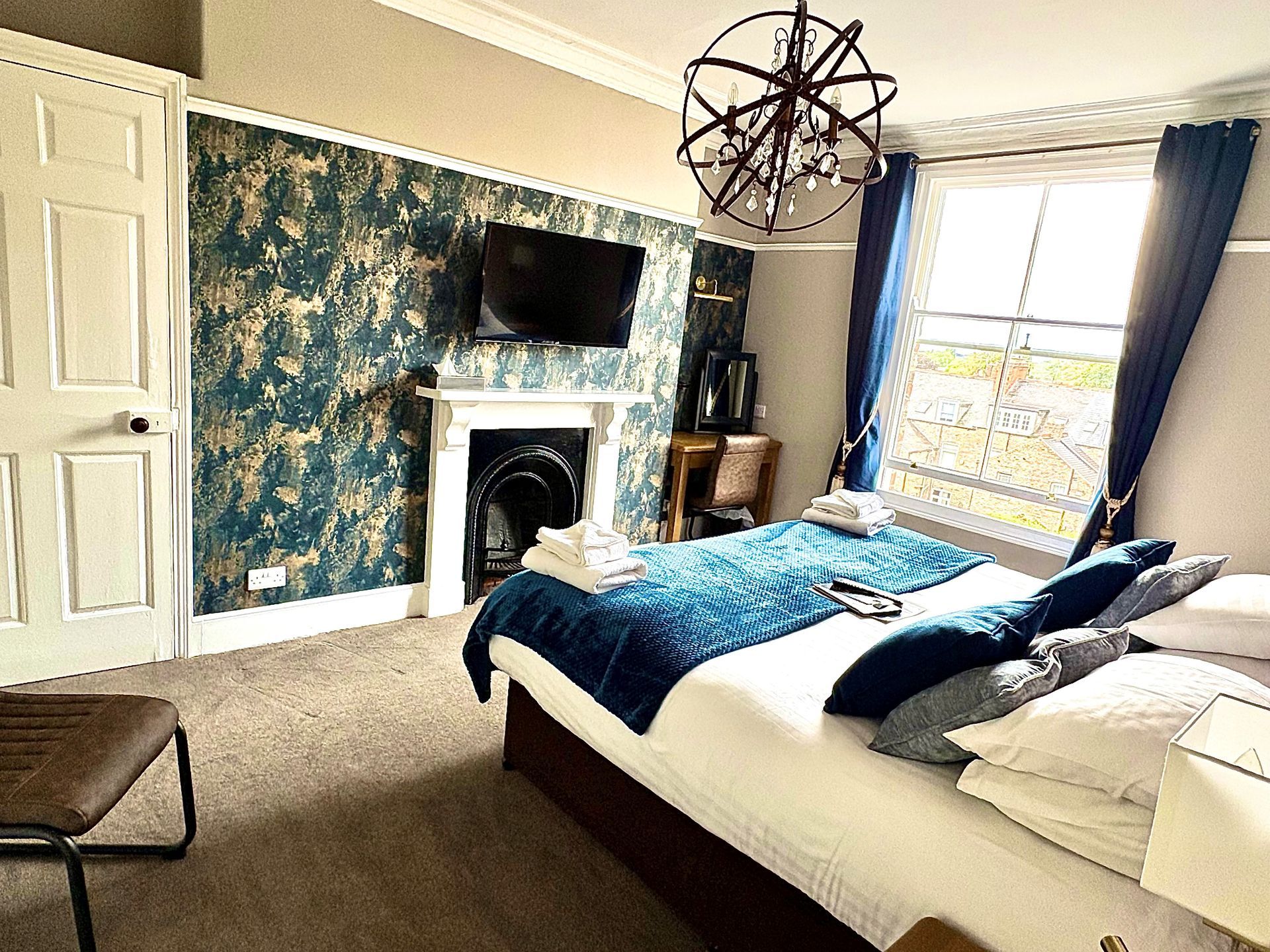 Bedroom with bed, nightstands, mirror, window, blue accents, and chandelier.