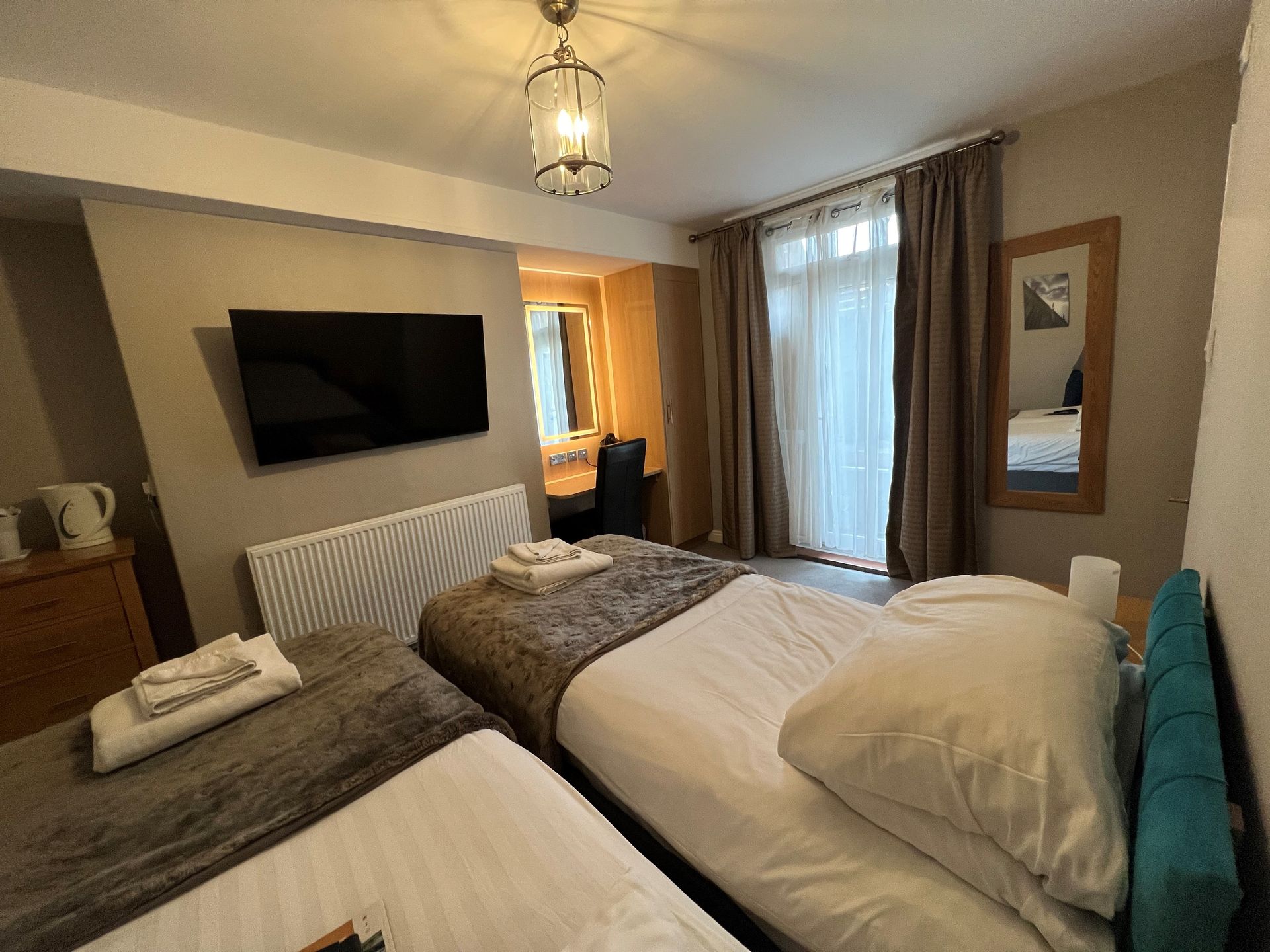 Twin bedroom with two beds, red armchair, TV, and large window with natural light.