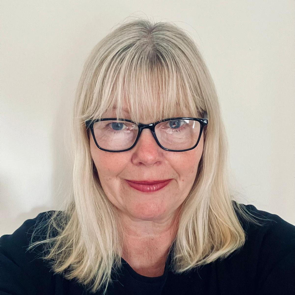 hotel reception. Woman with blonde hair and glasses smiles, wearing a black top.