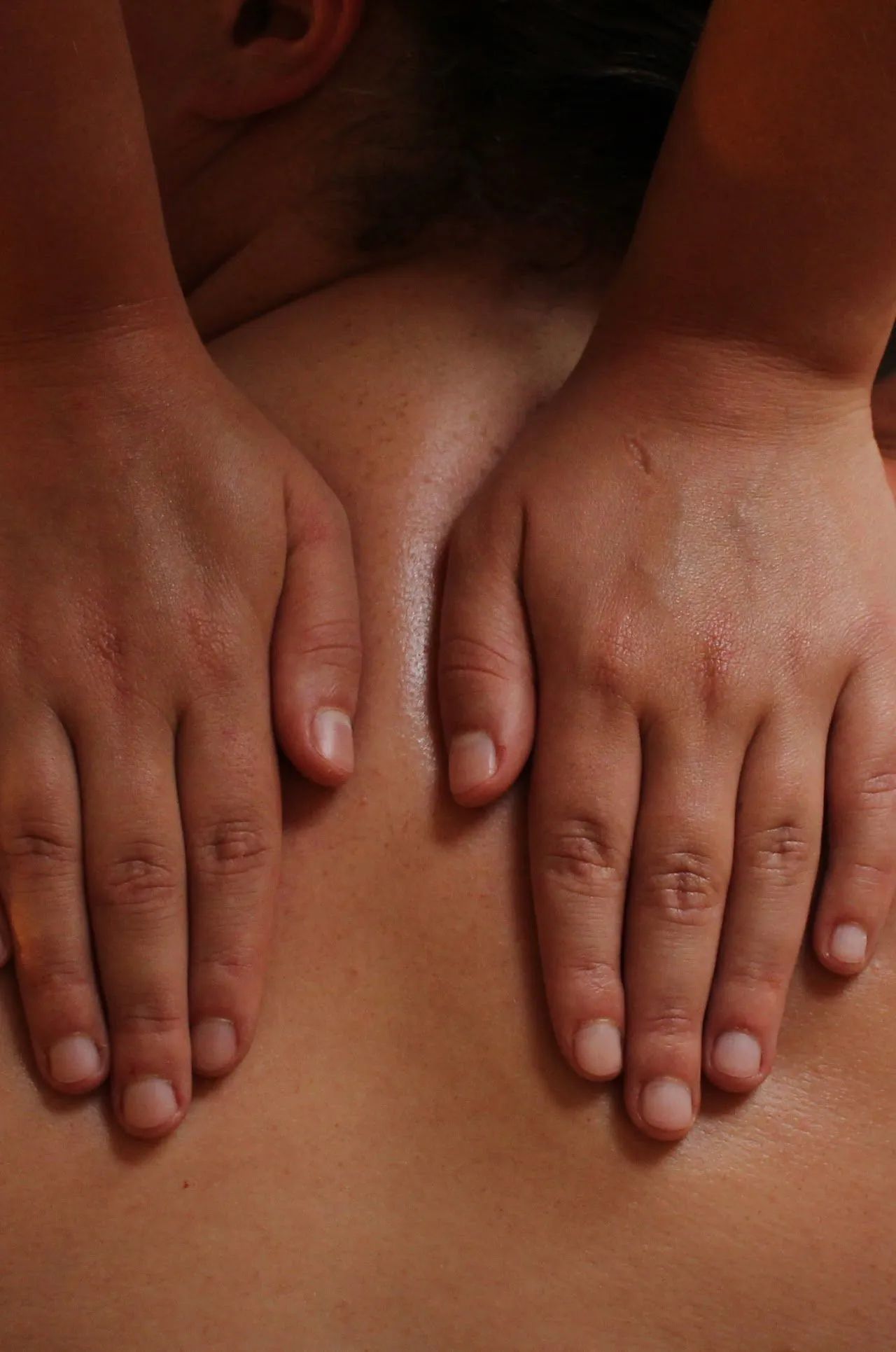 Hands performing a back massage on a person, with visible skin and oil.