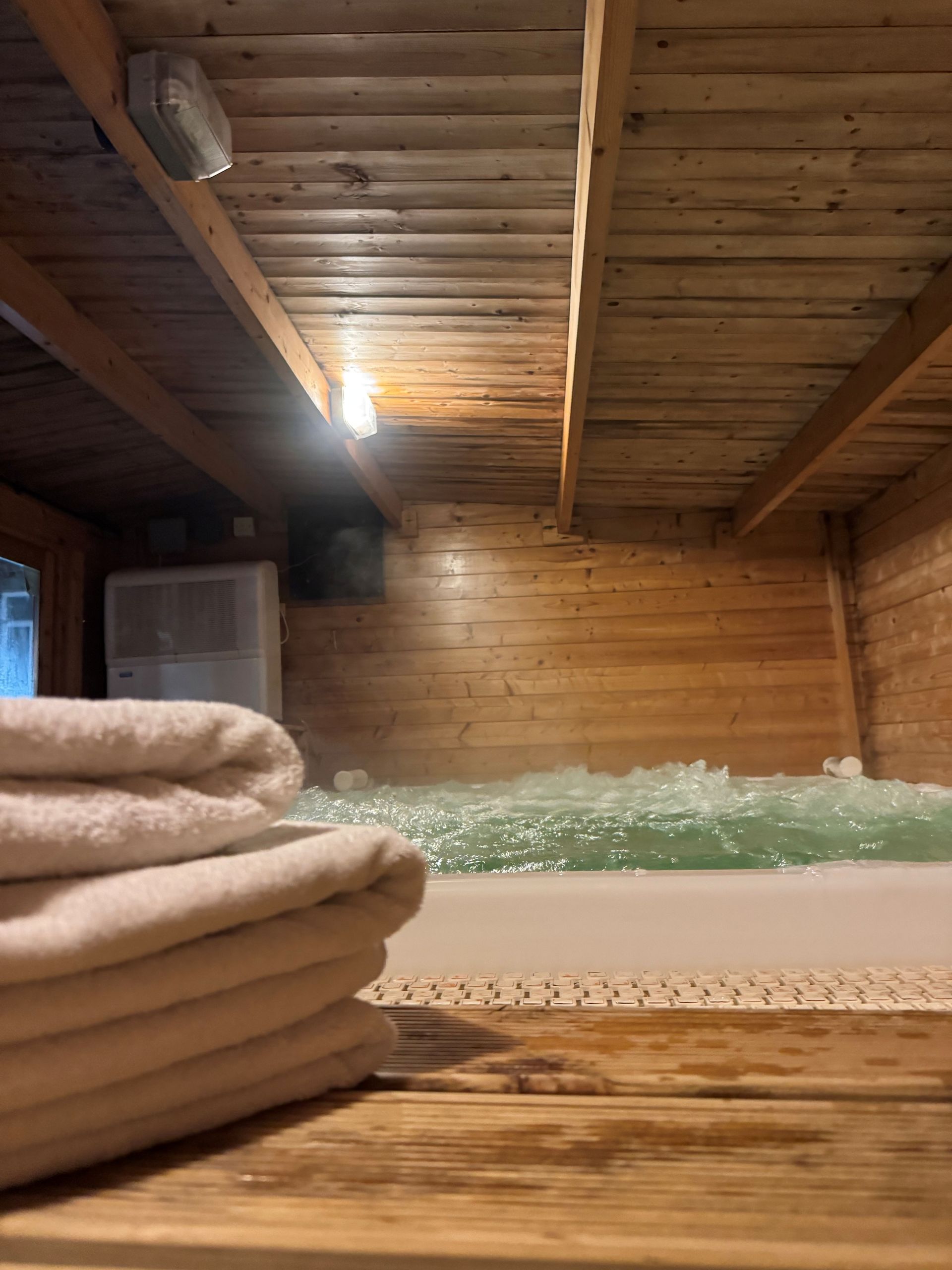 Indoor hot tub with wooden paneling and towels on shelves.