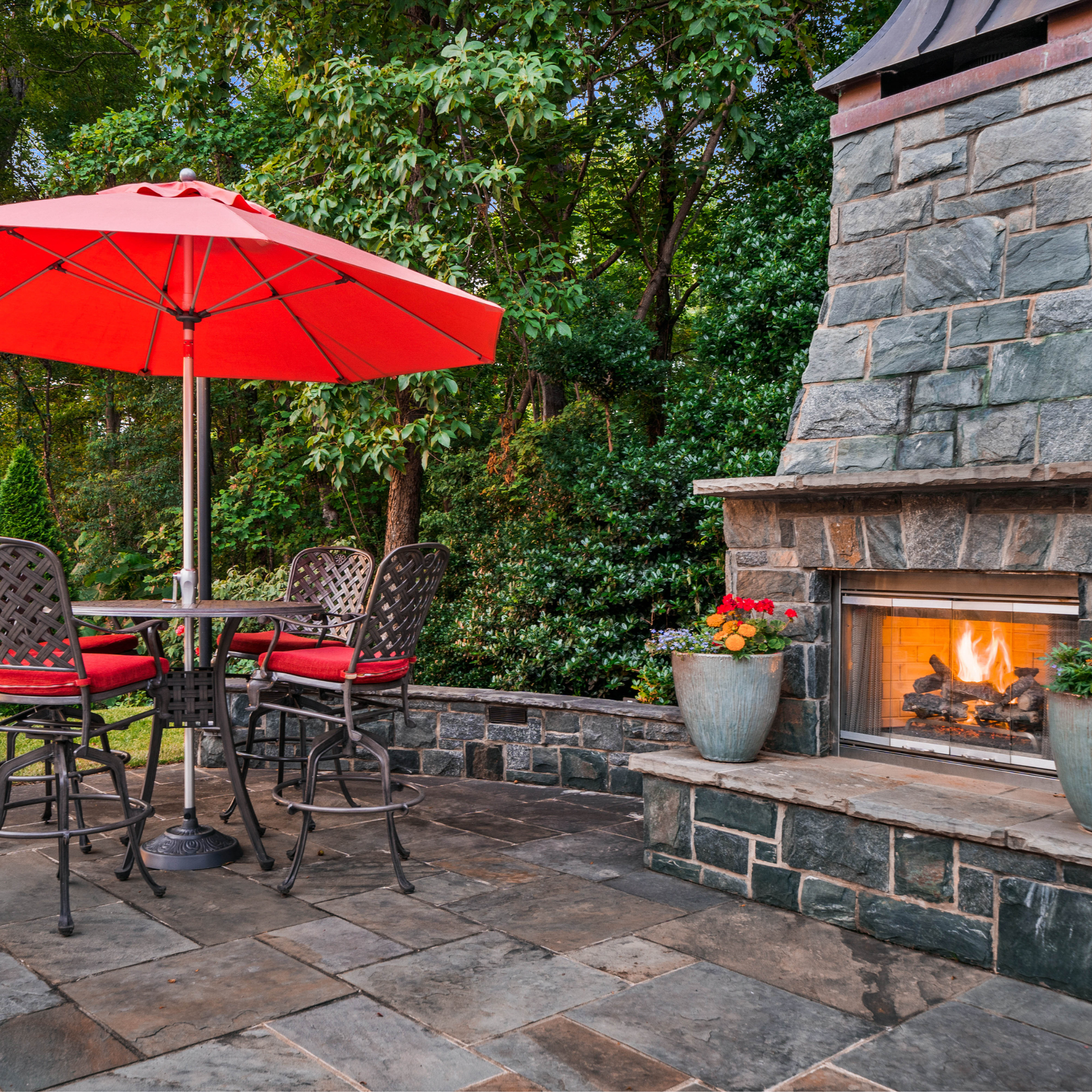 A red umbrella sits on a patio next to a fireplace
