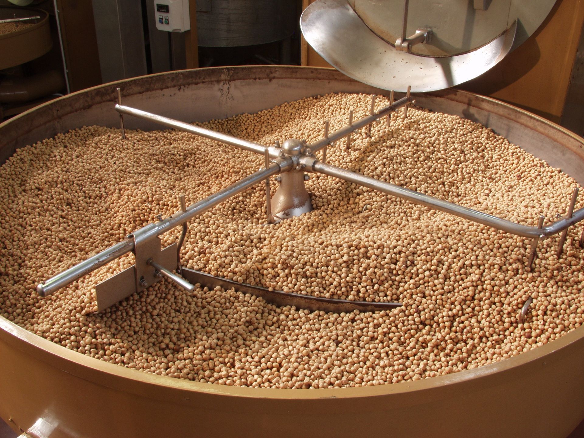 Grande macchina miscelatrice industriale con bracci di agitazione, riempita con piccoli oggetti beige simili a pellet.