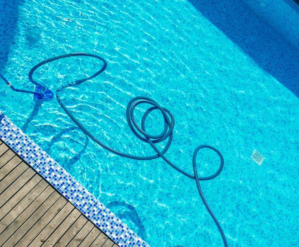 A hose is floating in a swimming pool next to a wooden deck