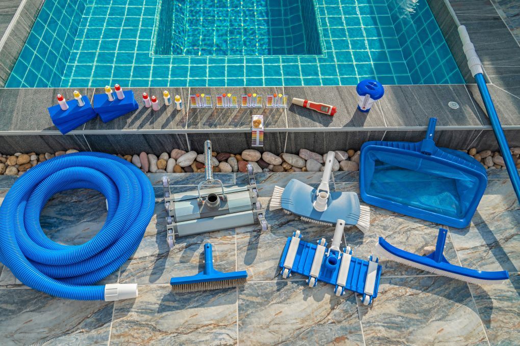 A bunch of swimming pool cleaning tools are sitting next to a swimming pool.